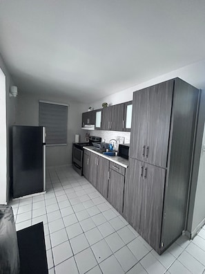 A compact kitchen with grey cabinets, a black refrigerator, and a tiled floor. - Nice and accessible apartment in San Juan area, very walkable distance to malls. (San Juan)