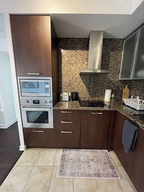 A modern kitchen with built-in appliances, a granite countertop, and a patterned rug. - The Entertainment District - York Suites (Toronto)