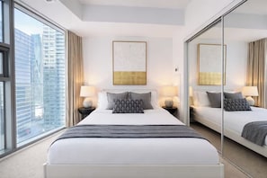 Een hotelkamer met een groot bed, twee nachtkastjes, een spiegel en uitzicht op de stad.
