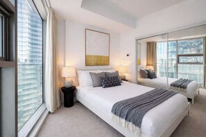 A modern hotel room with a large bed, bedside lamps, a mirror, and a city view. - The Entertainment District - York Suites (Toronto)
