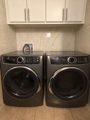 Two front-loading washing machines with control panels, placed side by side in a kitchen with white cabinets above. - Cozy Stay • Large Bedrooms • Smart TV • Parking (Montréal)