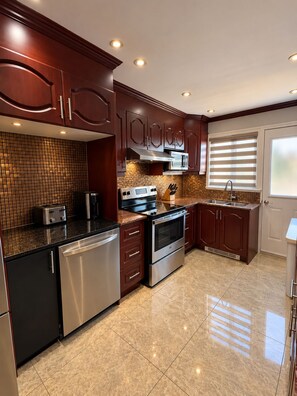 A modern kitchen with stainless steel appliances, dark wooden cabinets, and a tiled backsplash. - Cozy Stay • Large Bedrooms • Smart TV • Parking (Montréal)