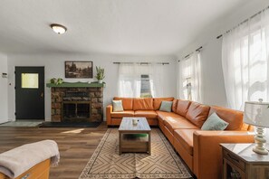 Een woonkamer met een open haard, een hoekbank, een salontafel en een vloerkleed.