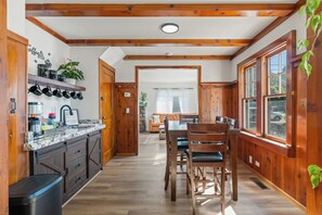 A kitchen with wooden beams, a marble countertop, and a dining area with a table and chairs. - Bright Mt. Shasta Cottage - Hot Tub, Patio & Coffee Bar (Mount Shasta)