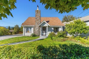 Een gelijkvloers huis met een stenen schoorsteen, een voortuin en een verzorgd gazon.