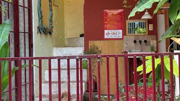 Un patio con una reja metálica roja, suelo de baldosas y pared amarilla con un cuadro enmarcado.