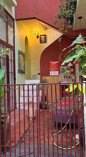 A courtyard with a red metal gate, a tiled floor, and a yellow wall with a framed picture. - Cozy 1-bedroom cottage in peaceful Thanh Khê with AC (Thanh Khê)