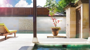 Eine Holzterrasse mit Pool, einem Holzstuhl und einem Blumentopf mit rosa Blüten.