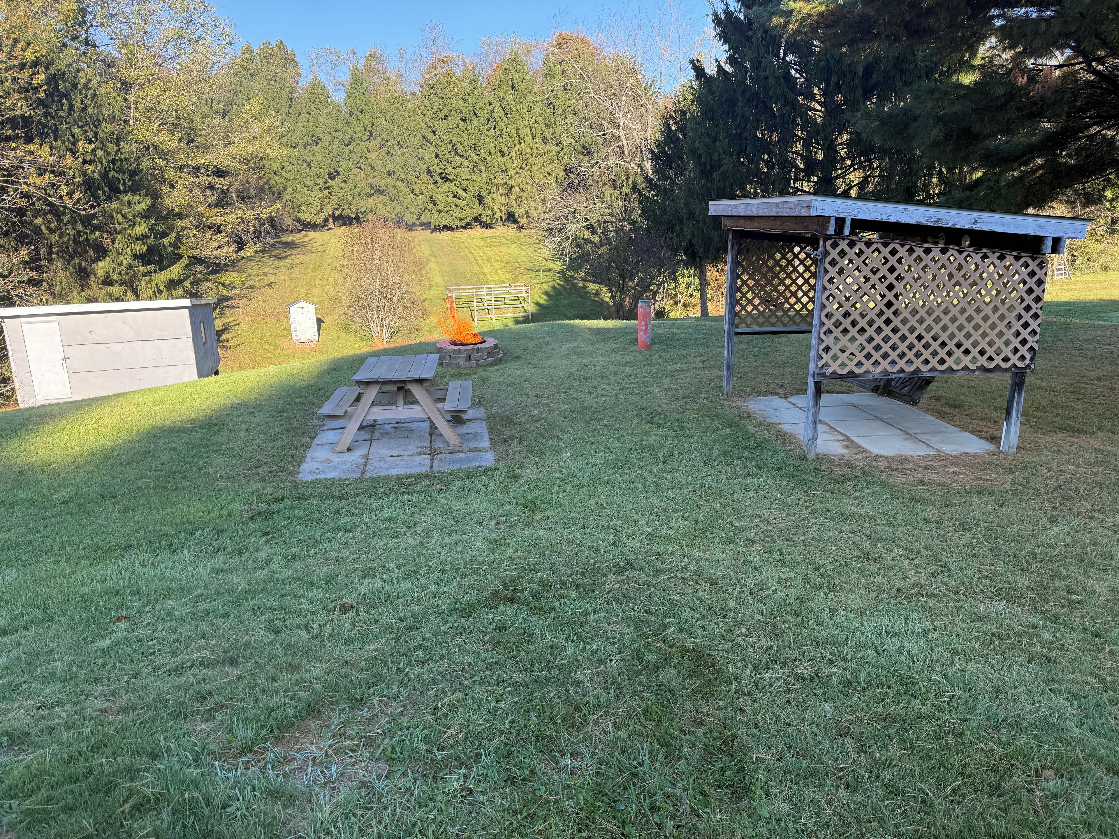 A backyard with a picnic table, a fire pit, and a wooden structure.