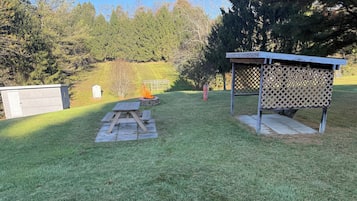 A backyard with a picnic table, a fire pit, and a wooden structure.