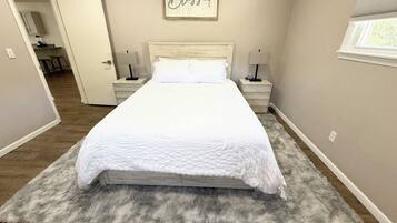 Un dormitorio con una cama grande, dos mesitas de noche, una lámpara de pared y un cartel enmarcado sobre la cama.