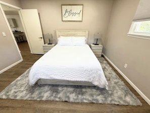 Quarto com uma cama grande, duas mesas de cabeceira, uma luminária na parede e uma placa emoldurada acima da cama.