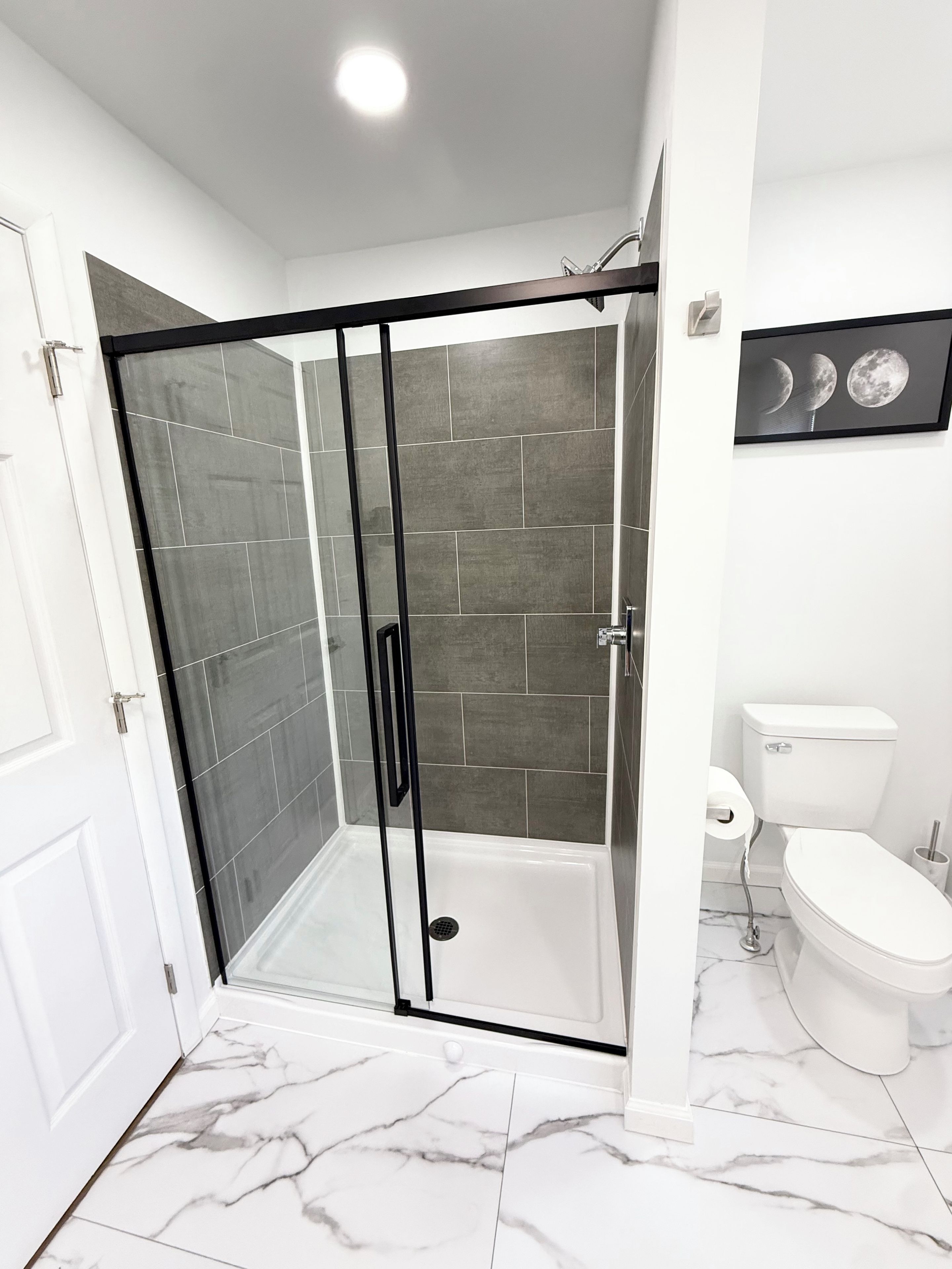 A modern bathroom with a glass-enclosed shower, white toilet, and marble flooring.