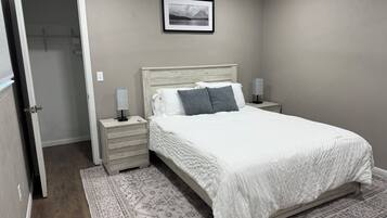 A bedroom with a bed, bedside tables, a nightstand, a rug, and a framed picture on the wall.