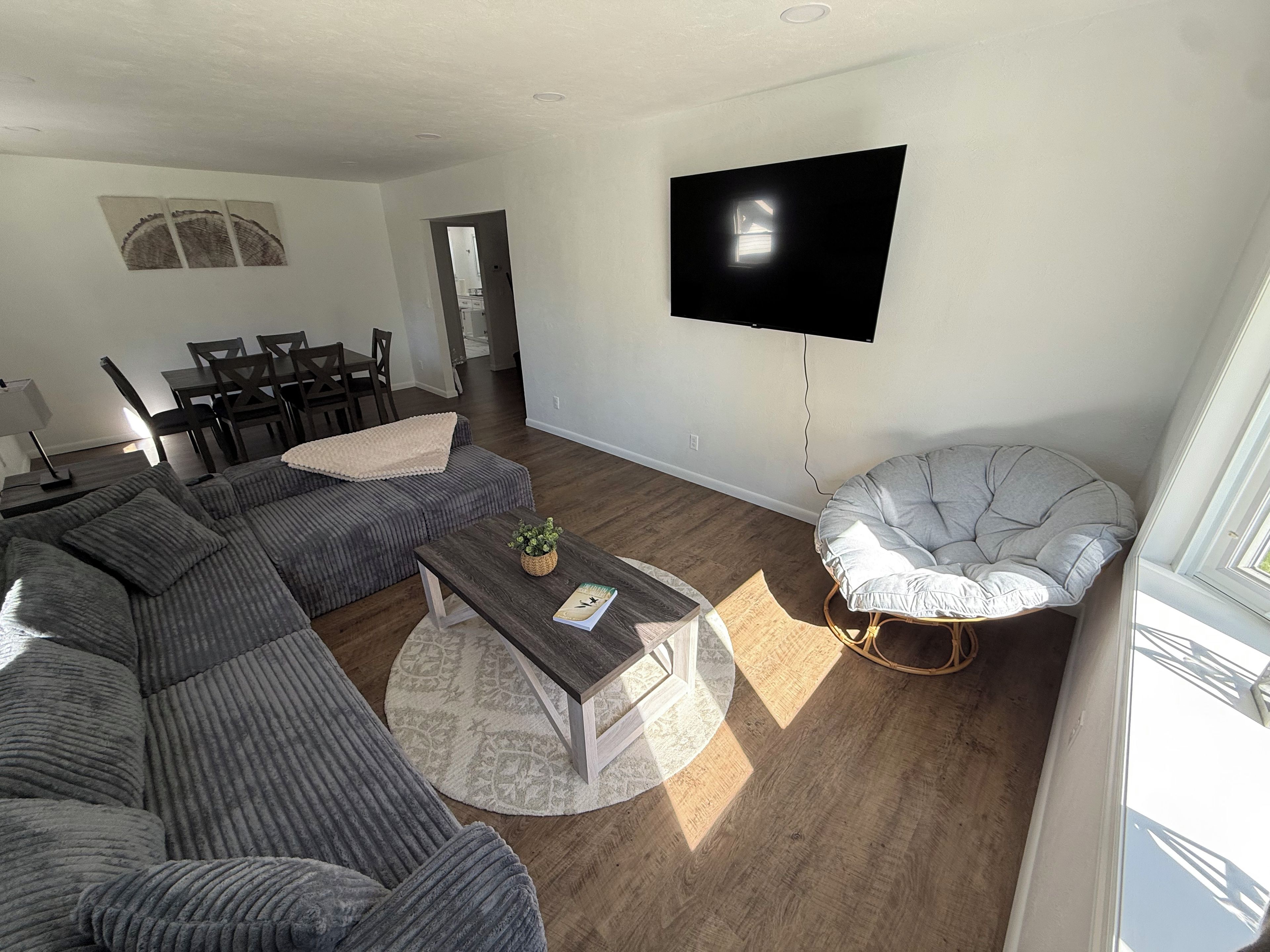 Una sala moderna con un sofá modular, una mesa de centro redonda, un sillón gris y un televisor de pantalla plana montado en la pared.