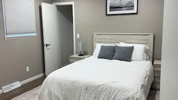 Ein Schlafzimmer mit einem Bett, Deckenventilator, Nachttisch, Nachttischlampe, einem Fenster mit Jalousien und einem gerahmten Bild an der Wand.