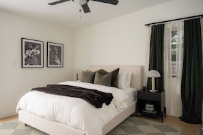Een slaapkamer met een bed, een nachtkastje, een lamp, een plafondventilator en twee ingelijste foto's aan de muur.