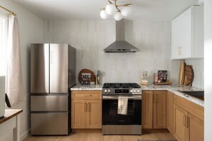 Eine moderne Küche mit einem Edelstahl-Kühlschrank, einem Gasherd, Holzschränken und einer Marmorarbeitsplatte.