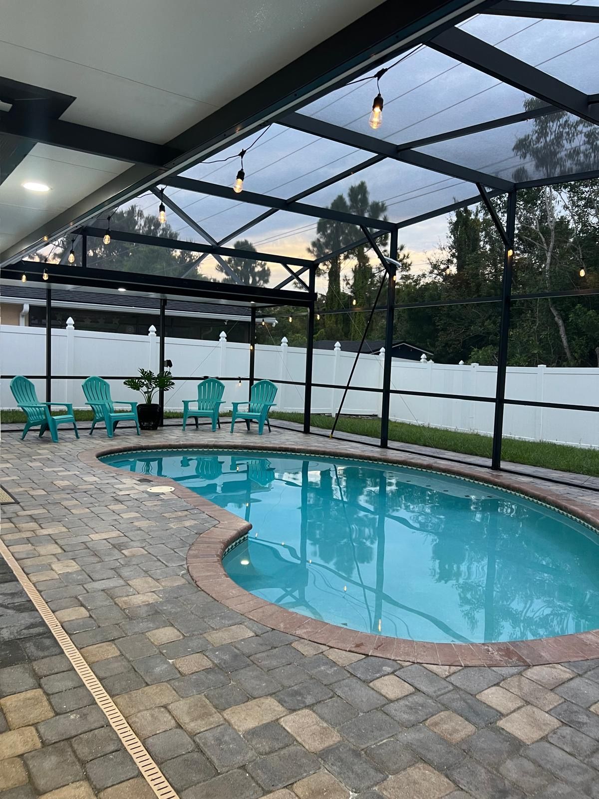 An outdoor swimming pool with a glass ceiling, surrounded by green chairs and a white fence.