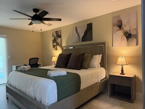 Ein Hotelzimmer mit Bett, Deckenventilator, Nachttisch mit Lampe und abstrakten Wandbildern.