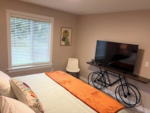 A hotel room with a bed, a television on a stand, a bicycle, and a window with blinds.