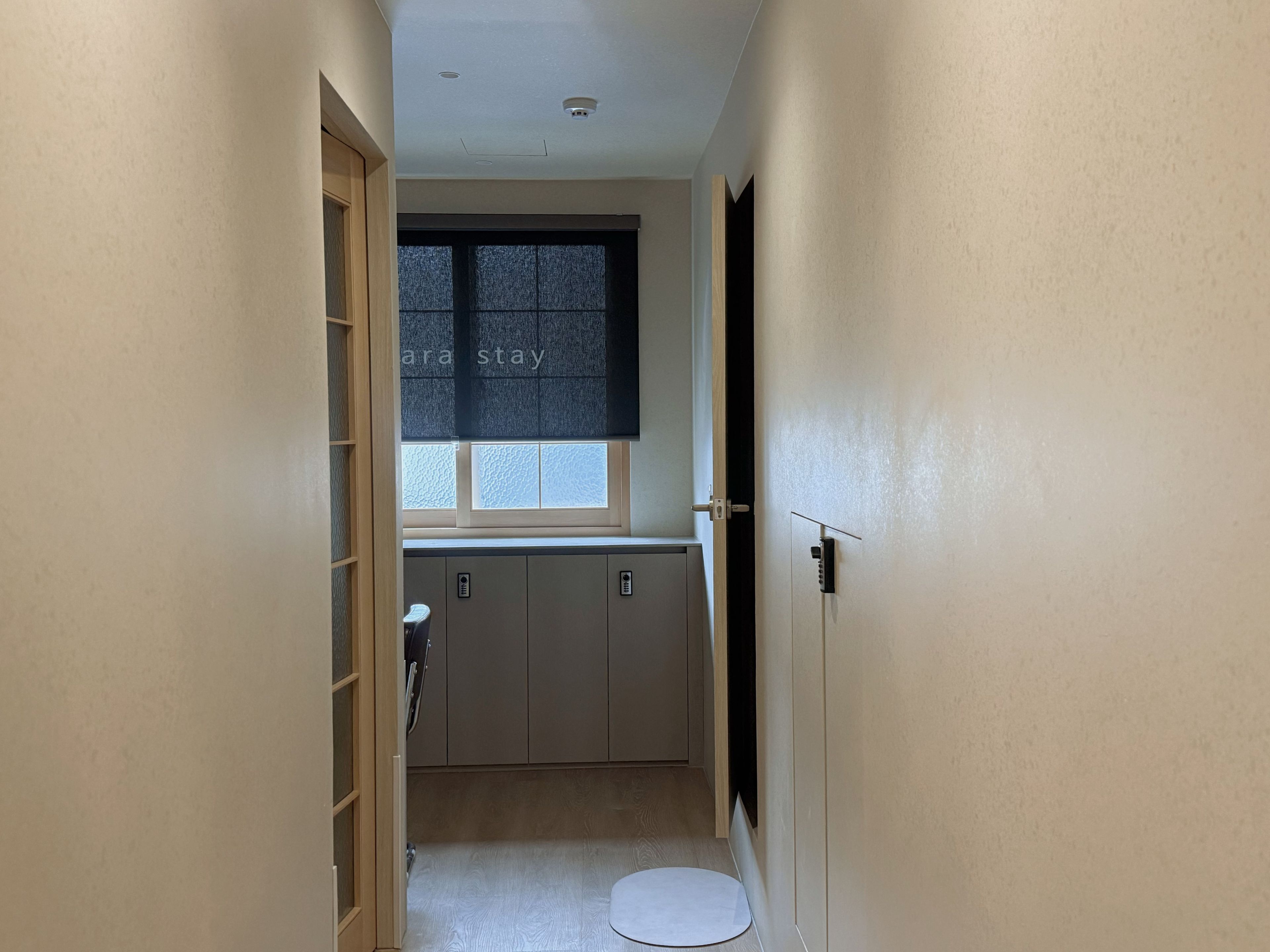 A narrow hallway leading to a small kitchenette with a window, a door, and a toilet.