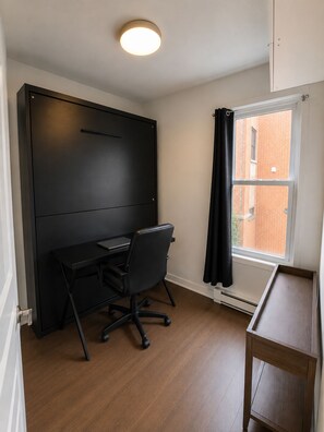 Ein Zimmer mit Schreibtisch, Stuhl und einem Vorhangfenster.