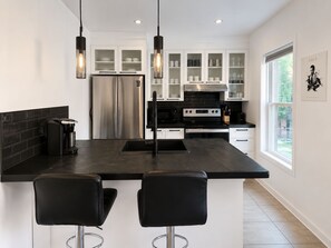 Une cuisine moderne dotée d’un îlot central, d’appareils électroménagers en acier inoxydable et de tabourets de bar noirs.