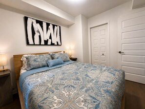 Une chambre à coucher comprenant un lit, des tables de chevet, une œuvre d’art accrochée au mur et une porte.