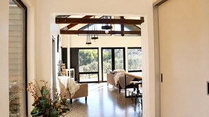A modern interior with a high ceiling, large windows, a seating area with a sofa and a table, and a plant.