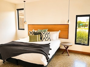 A bedroom with a bed, bedside table, and a window with a view of greenery. - Villa Rochford Kellevie (Sorell)