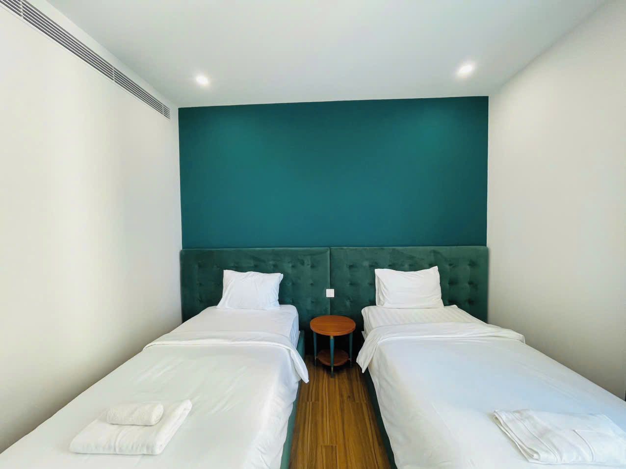 A hotel room with two single beds, a round table, and a teal accent wall.