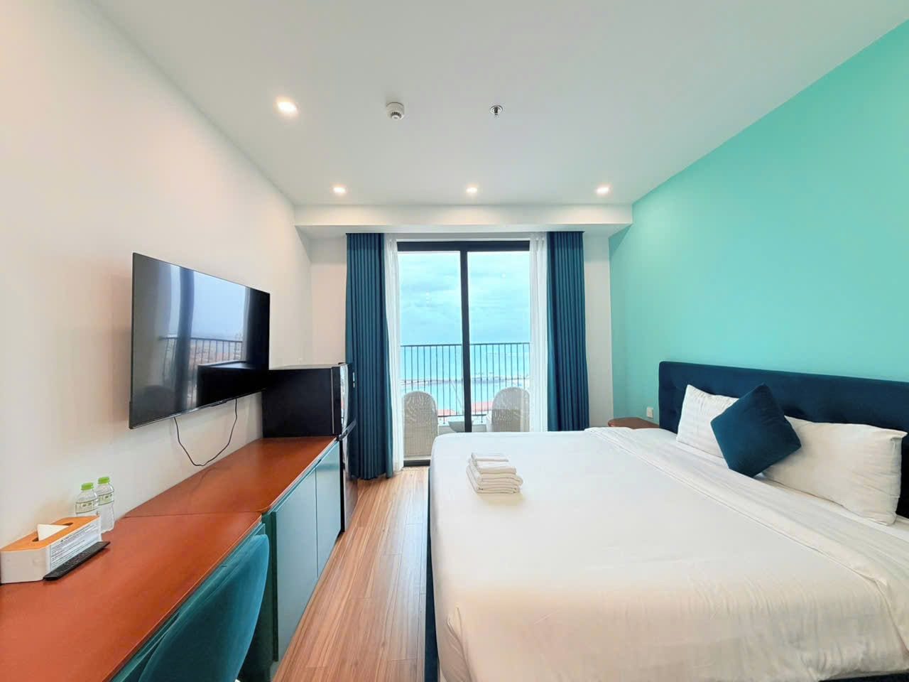 A hotel room with a bed, a desk, a TV, and a balcony with a view.