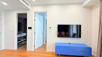 A modern living room with a wooden floor, a blue bench, a flat-screen TV mounted on the wall, and a door leading to a closet.