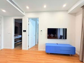 Una sala de estar moderna con suelo de madera, un banco azul, un televisor de pantalla plana montado en la pared y una puerta que da a un armario.