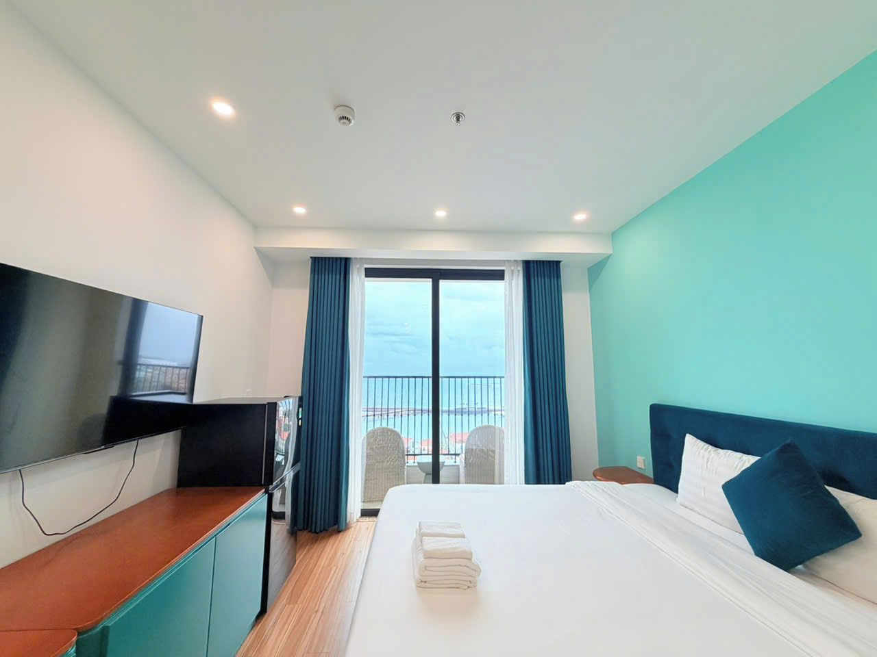 Habitación de hotel con cama, televisión, escritorio y balcón con vistas.