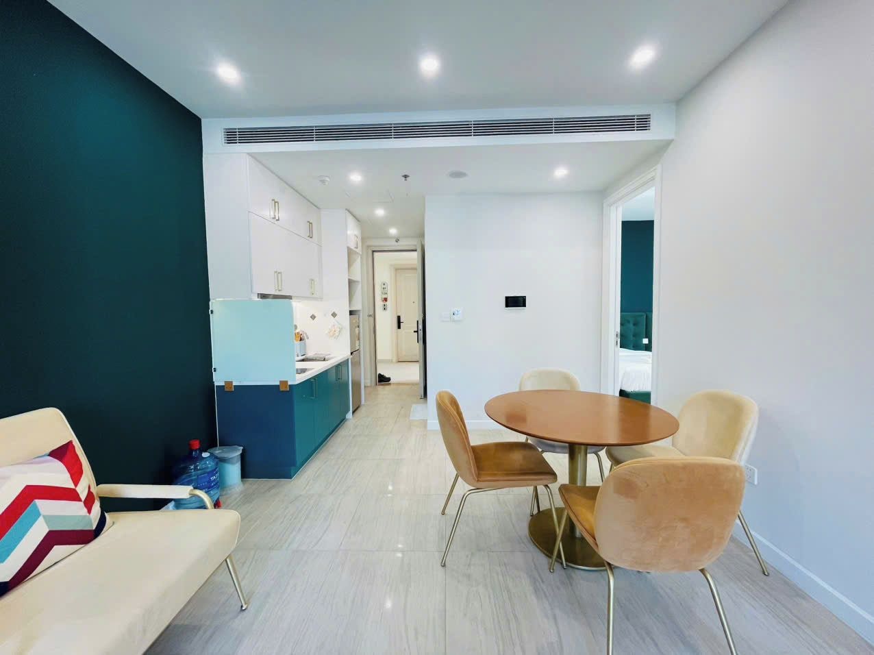 A modern living room with a sofa, a dining table with chairs, and a kitchen area in the background.