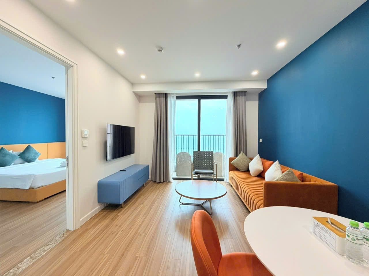 A hotel room with a bed, a sofa, a dining table, and a TV.
