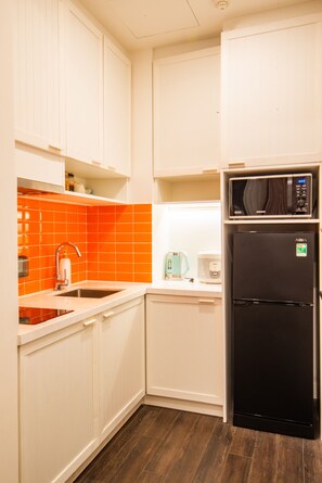 A compact kitchen with white cabinets, an orange-tiled backsplash, a black refrigerator, and a microwave on top. - VietStay Vietnam (Phu Quoc)