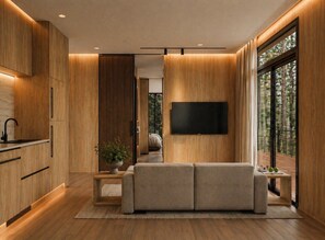 A modern living room with a flat-screen TV, wooden flooring, and a large window offering a view of trees. - Private 1BR Mountain Cabin with Hot Tub & Views (Menlo)