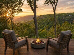 Une terrasse avec deux chaises donnant sur un foyer extérieur, et offrant une vue sur un paysage boisé.