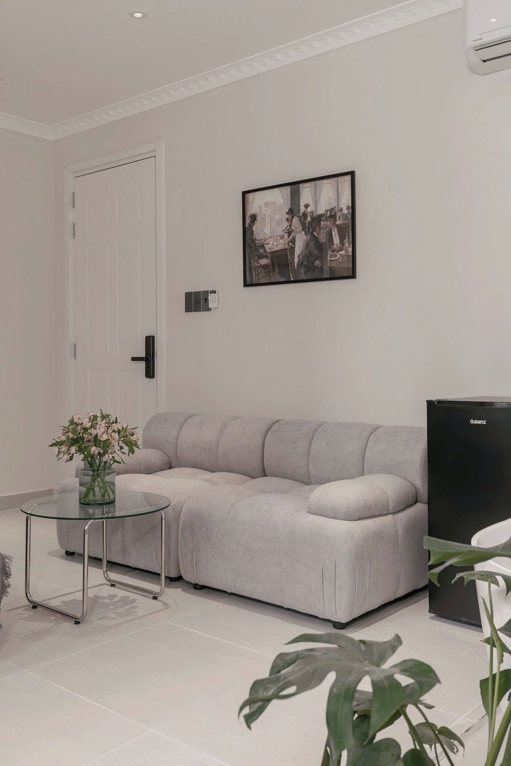 Una sala moderna con un sofá gris, una mesa de centro de vidrio, un cuadro enmarcado y un televisor negro.