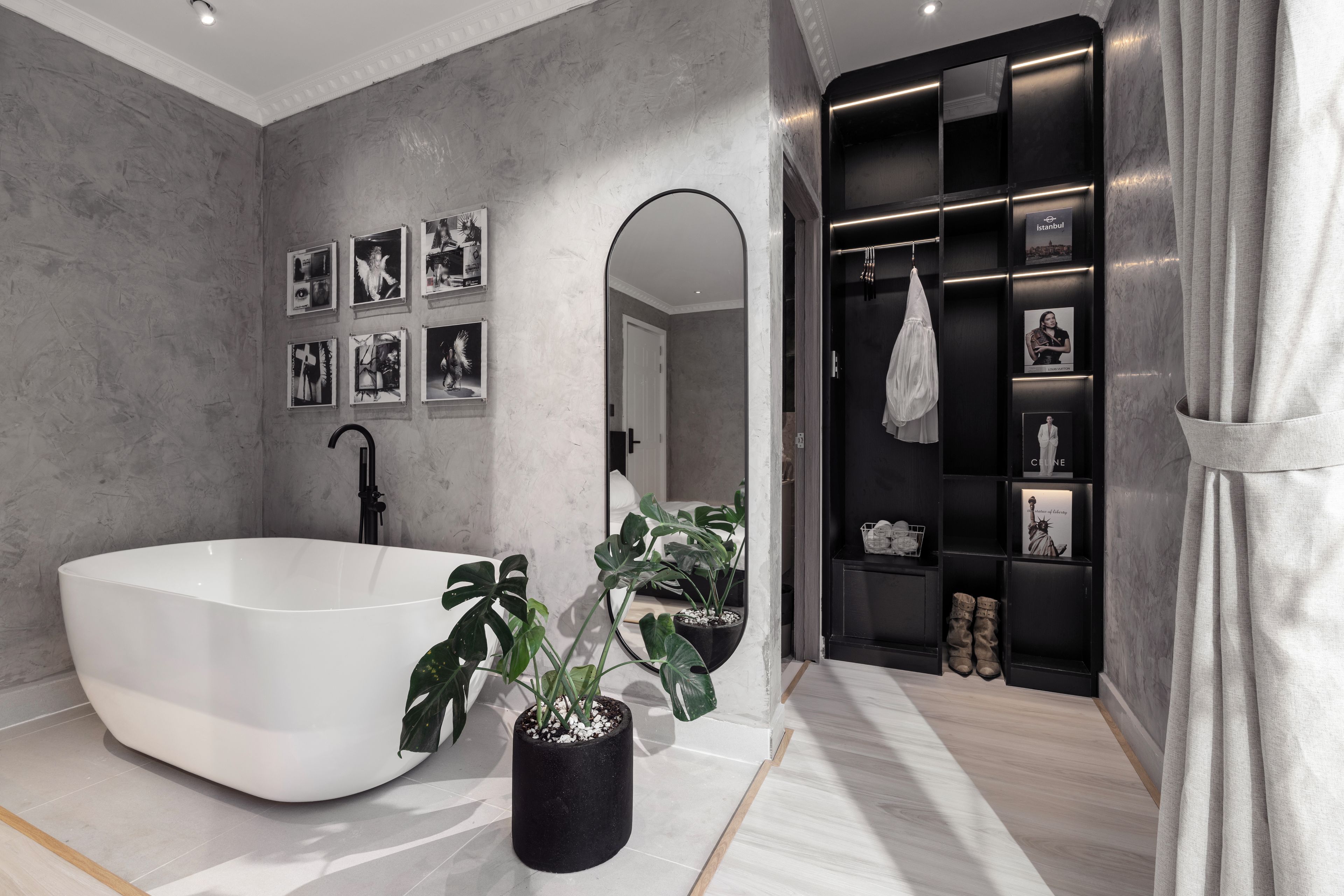 A modern bathroom with a freestanding bathtub, a large mirror, and a vanity with a black shelf displaying various items.