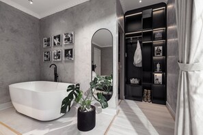Une salle de bain moderne avec une baignoire sur pieds, un grand miroir et un meuble-lavabo doté d’une étagère noire où sont exposés divers objets.