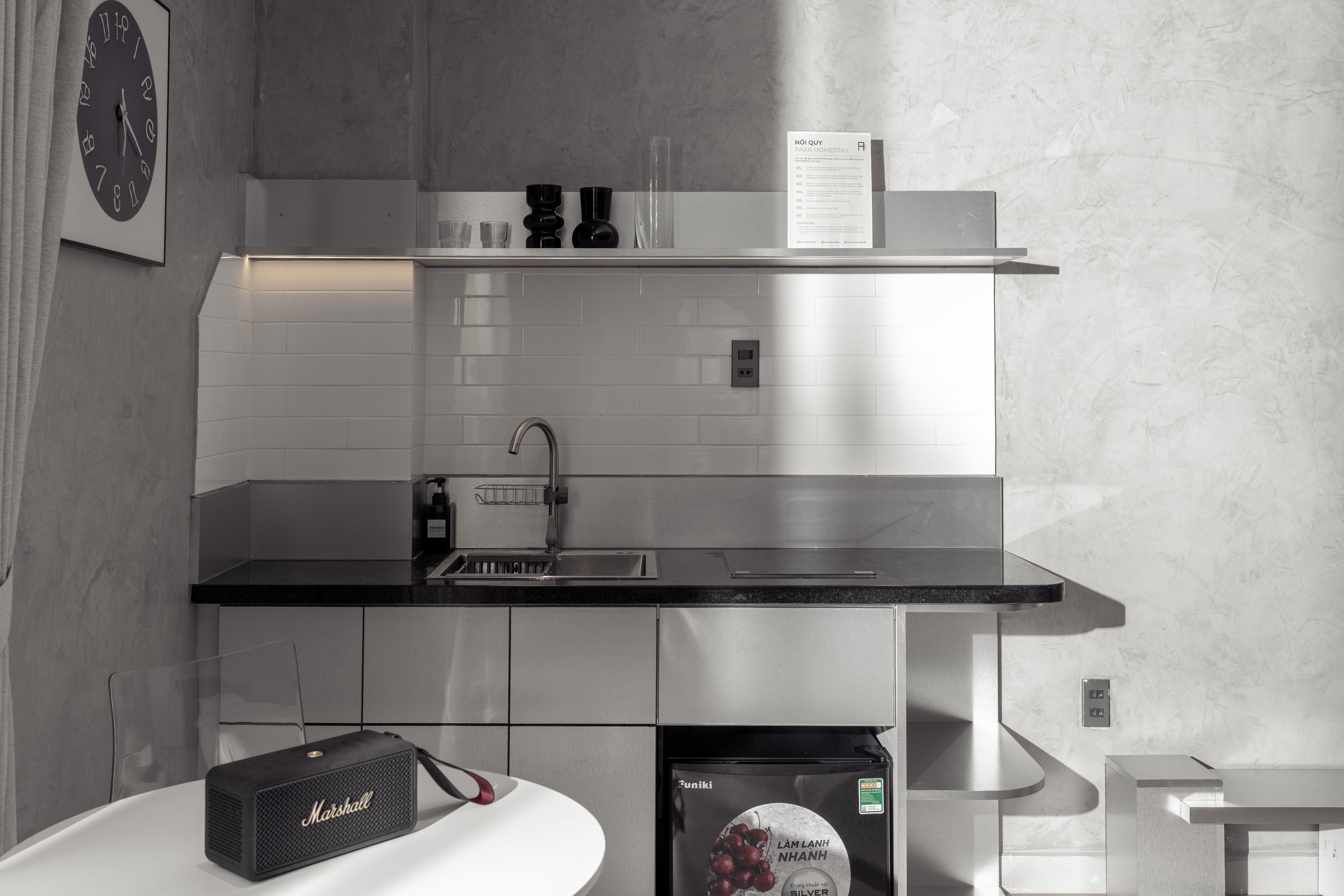 Una cocina moderna con encimera negra, electrodomésticos de acero inoxidable y salpicadero de azulejos blancos.