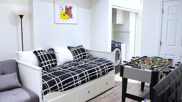 Une chambre avec un lit, un fauteuil gris, une table de baby-foot, un lave-linge et une œuvre d’art représentant un papillon, encadrée et accrochée au mur.