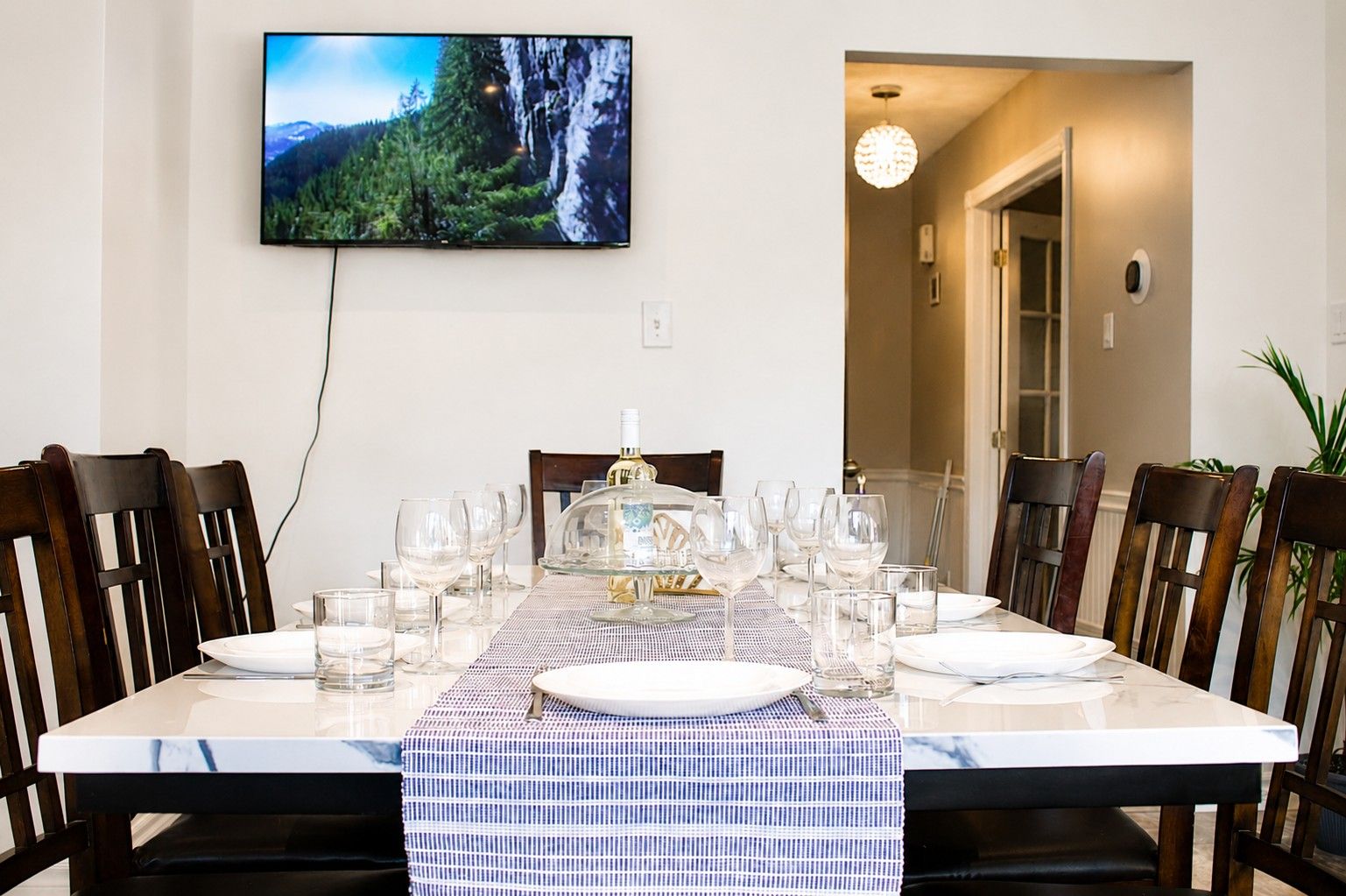 Un coin repas avec une table dressée pour six personnes, un téléviseur fixé au mur et une vue sur un paysage montagneux.