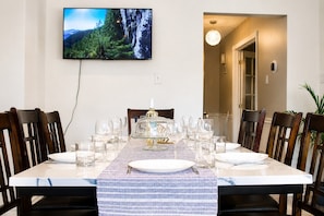 A dining area with a table set for six, a television mounted on the wall, and a view of a mountainous landscape.