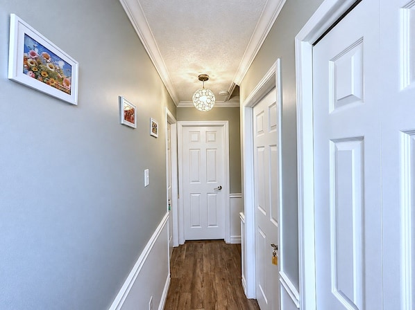 A hallway with white doors, a ceiling light fixture, and framed pictures on the wall.