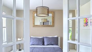A bedroom with a bed, a hanging light fixture, a mirror, and a window with blinds.